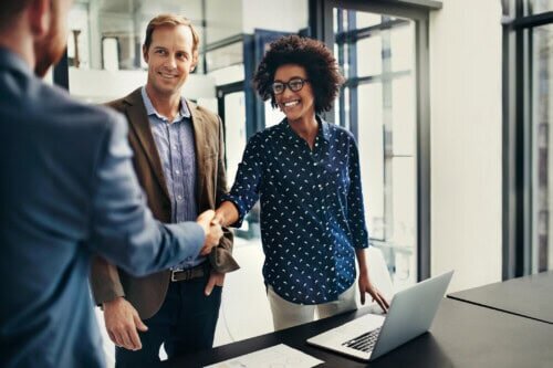 Smiling couple shaking hands with a real estate professional in an office, finalizing a home sale deal.