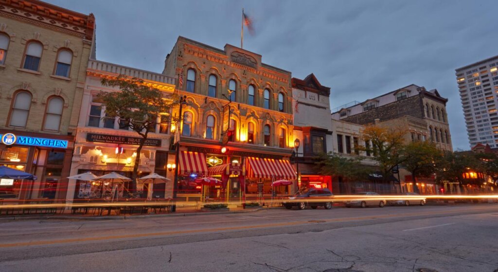 Street view of the Milwaukee Brat House at night with illuminated signs and buildings.