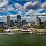 A scenic aerial view of downtown Milwaukee, Wisconsin, showcasing the skyline, Lake Michigan shoreline, and the Milwaukee Art Museum under a vibrant, cloud-filled sky.