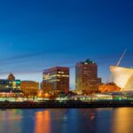 Milwaukee skyline at dusk featuring the illuminated Milwaukee Art Museum and surrounding city buildings reflected on Lake Michigan.