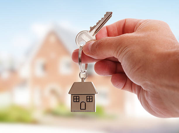 A hand holding a key with a house-shaped keychain, symbolizing the transition of ownership in the home-selling process.