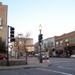 Downtown Oshkosh, Wisconsin, showing a busy street corner with historic brick buildings, storefronts, and traffic lights at dusk.