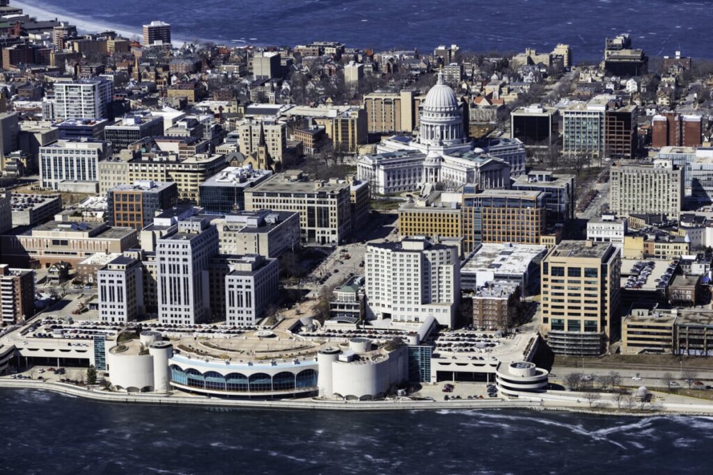Aerial view of downtown Madison, Wisconsin, featuring the Wisconsin State Capitol building, surrounded by commercial buildings and bordered by a frozen lake.