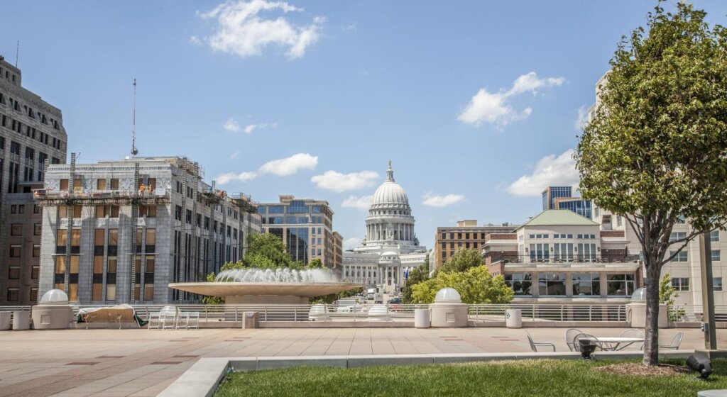 View of the Wisconsin State Capitol from Monona Terrace in Madison on a sunny day with blue skies and scattered clouds.