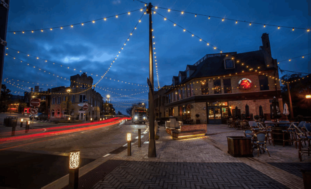 Downtown Wauwatosa at night with festive string lights and a cozy restaurant, ideal for those selling a house during a divorce in Wauwatosa.