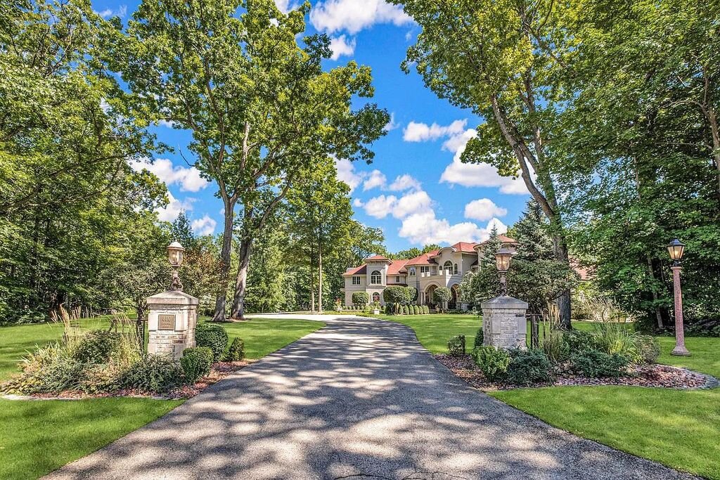 Luxurious Brookfield estate with gated driveway, manicured lawn, and grand architecture surrounded by tall trees under a bright blue sky.