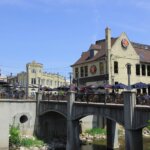 Outdoor dining on a sunny day in Wauwatosa’s historic Village district, with a scenic bridge and charming brick and cream-colored buildings in view.