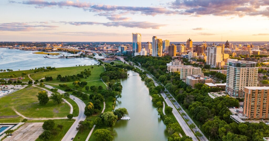 Aerial view of downtown Milwaukee at sunset, showing Lake Michigan, city skyline, and green parks along the river.