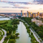 Aerial view of downtown Milwaukee at sunset, showing Lake Michigan, city skyline, and green parks along the river.