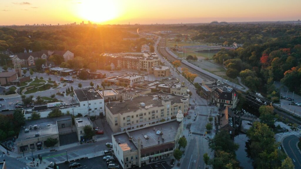 Aerial view of downtown Wauwatosa, Wisconsin at sunset, showing historic buildings, a train line, and surrounding trees.
