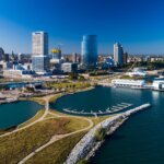 Aerial view of downtown Milwaukee, Wisconsin, showing the city skyline, Lake Michigan waterfront, Discovery World, and marina on a clear blue day.