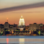 Madison skyline at dusk with the Wisconsin State Capitol illuminated and reflected on the lake.