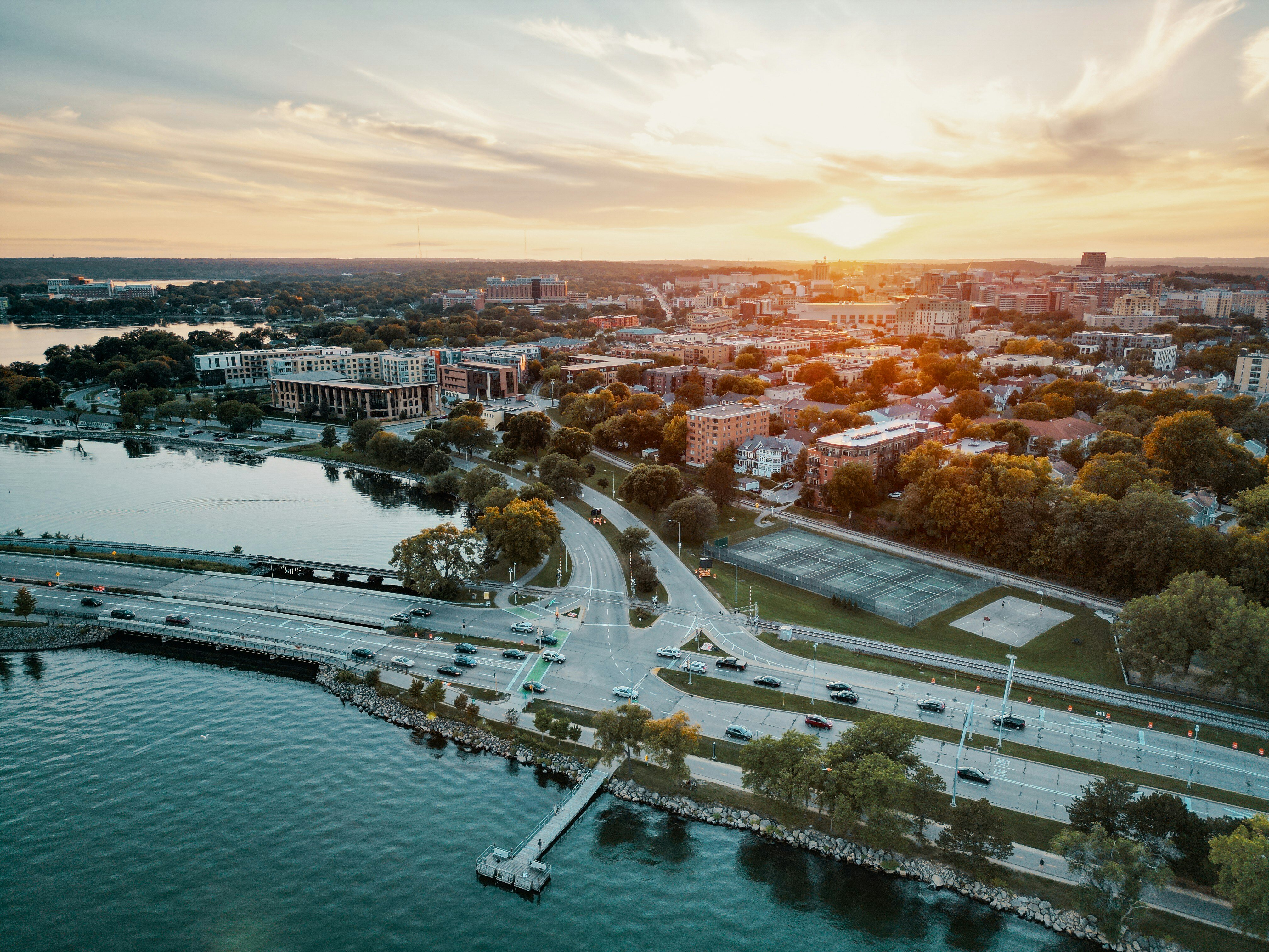 Aerial view of Madison, Wisconsin at sunset with roads, buildings, and lakeshore visible.