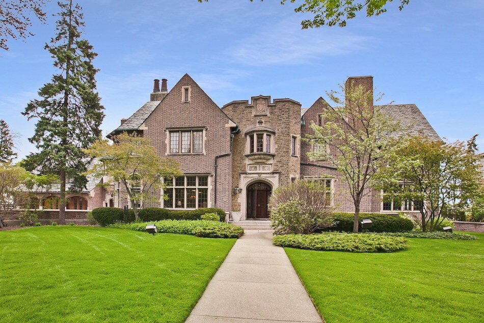 Elegant brick luxury estate with detailed stonework, manicured lawn, and grand entrance walkway.