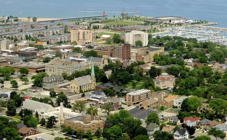 Aerial view of downtown Kenosha, Wisconsin, showcasing residential neighborhoods, historic churches, marina, and Lake Michigan shoreline in the background.