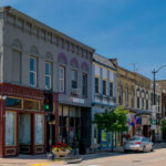 Historic downtown Brookfield, WI featuring colorful storefronts, parked cars, and a clear blue sky on a sunny day.