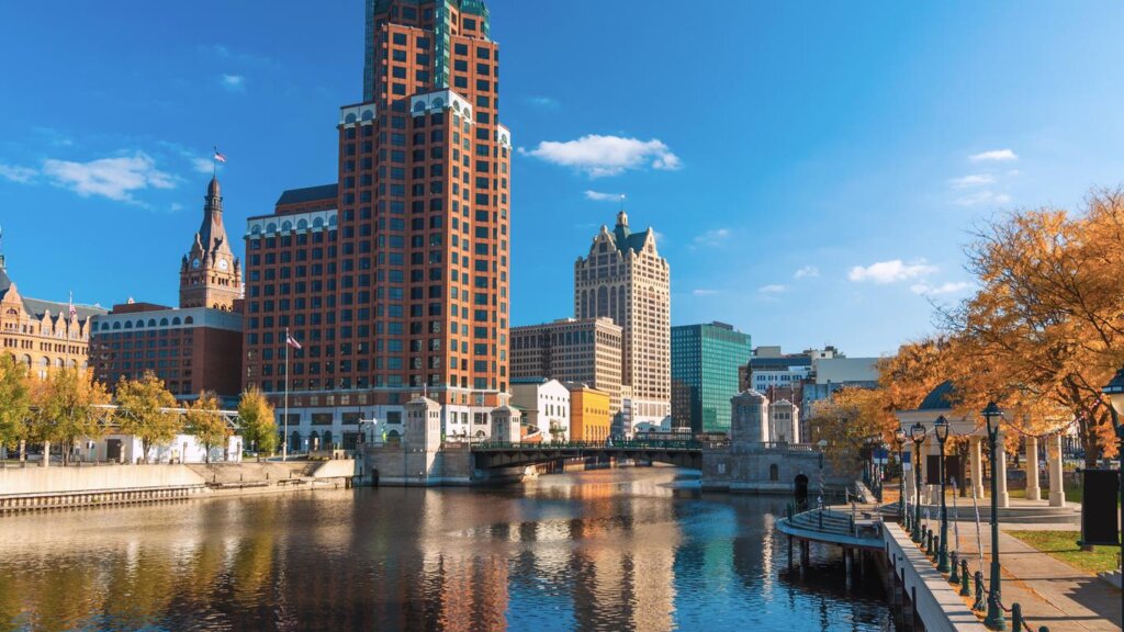 Downtown Milwaukee skyline with historic and modern buildings reflected in the river on a clear autumn day.