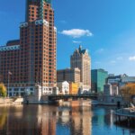 Downtown Milwaukee skyline with historic and modern buildings reflected in the river on a clear autumn day.