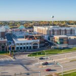 Aerial view of The Corners of Brookfield shopping and residential complex, featuring retail stores, apartments, and nearby highways under a clear blue sky.
