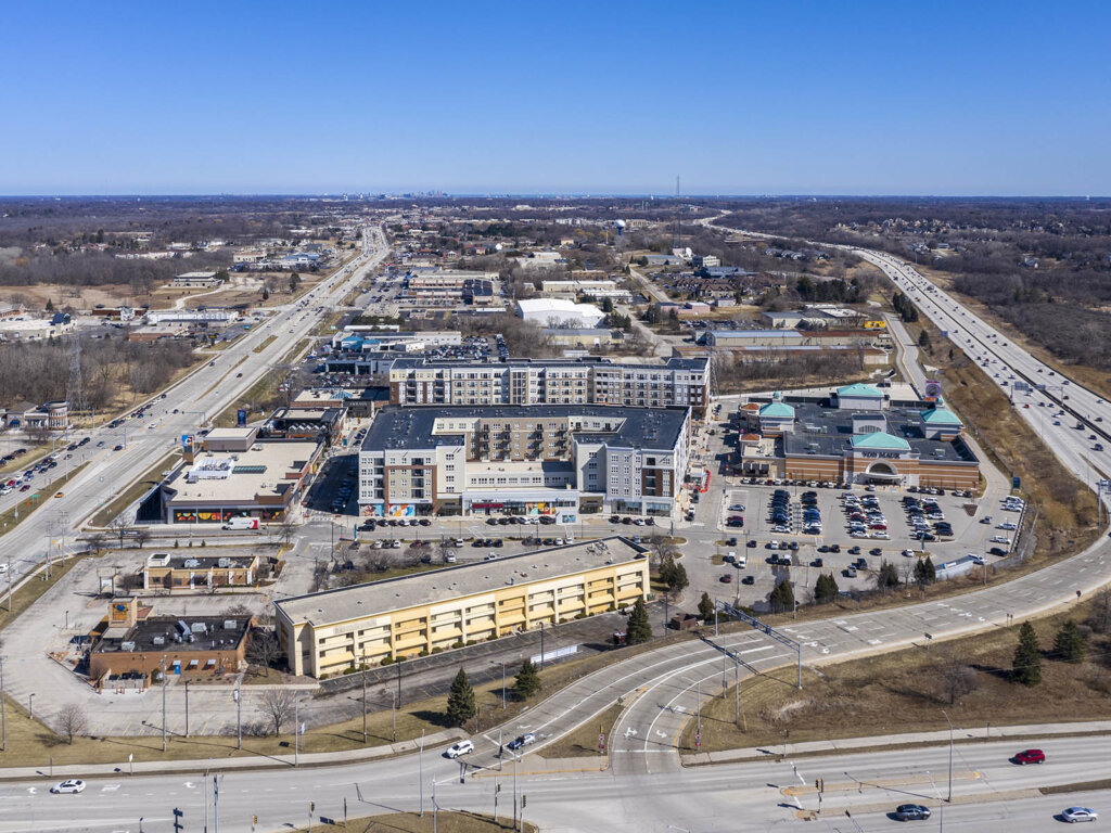 Aerial view of a commercial and residential area in Brookfield, Wisconsin, showing shopping centers, apartment buildings, and major highways.