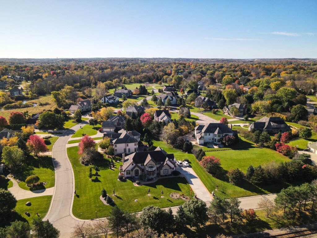 Aerial view of a suburban Brookfield neighborhood in autumn, featuring large single-family homes, colorful trees, and winding streets.