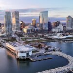 Aerial view of downtown Milwaukee skyline at sunset, featuring modern high-rise buildings, the Milwaukee Art Museum, and Lake Michigan shoreline.