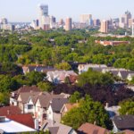 Aerial view of residential homes in Brookfield with the Milwaukee skyline in the background, surrounded by lush green trees under a clear sky.