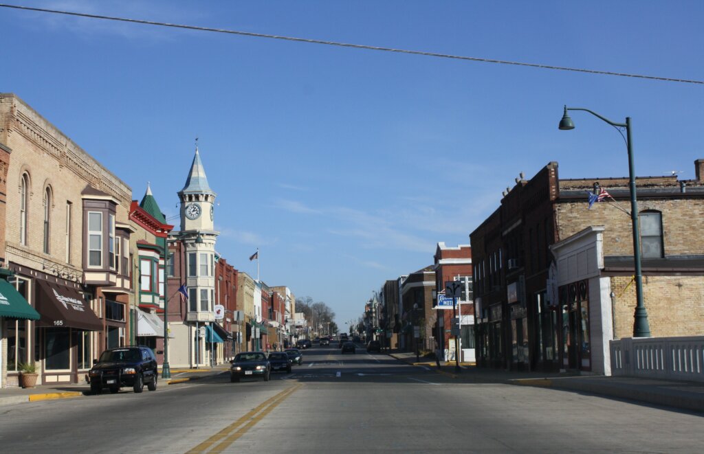 Downtown street view of Berlin, Wisconsin, featuring historic buildings, a clock tower, and cars under a clear blue sky.
