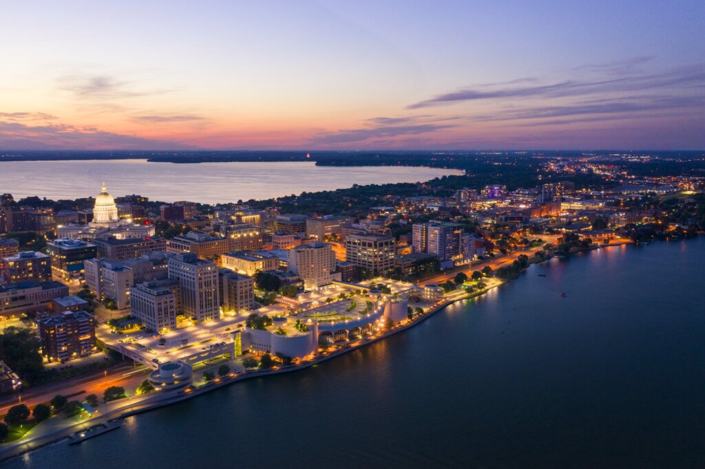 Aerial view of downtown Madison, Wisconsin at dusk, featuring the State Capitol and shimmering lakefront lights.
