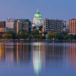 Evening skyline of downtown Madison, Wisconsin, with the State Capitol dome lit up and colorful city lights reflecting on the calm lake.