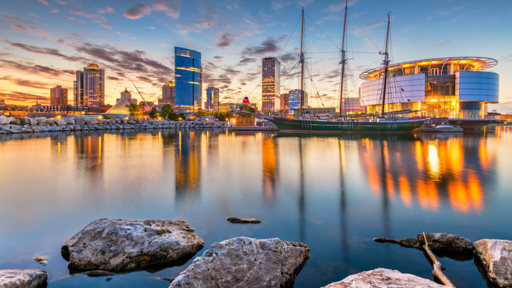 Sunset view of downtown Milwaukee skyline with sailboats and waterfront reflections.