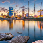 Sunset view of downtown Milwaukee skyline with sailboats and waterfront reflections.