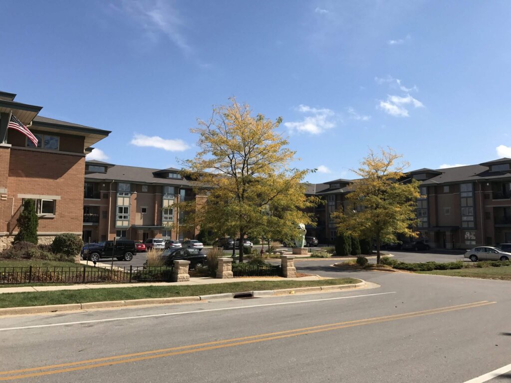 Modern apartment complex in New Berlin with parked cars, autumn trees, and clear blue skies.