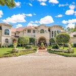 Luxurious estate home in Brookfield, WI featuring elegant architecture, manicured landscaping, and a grand arched entryway under a bright blue sky.