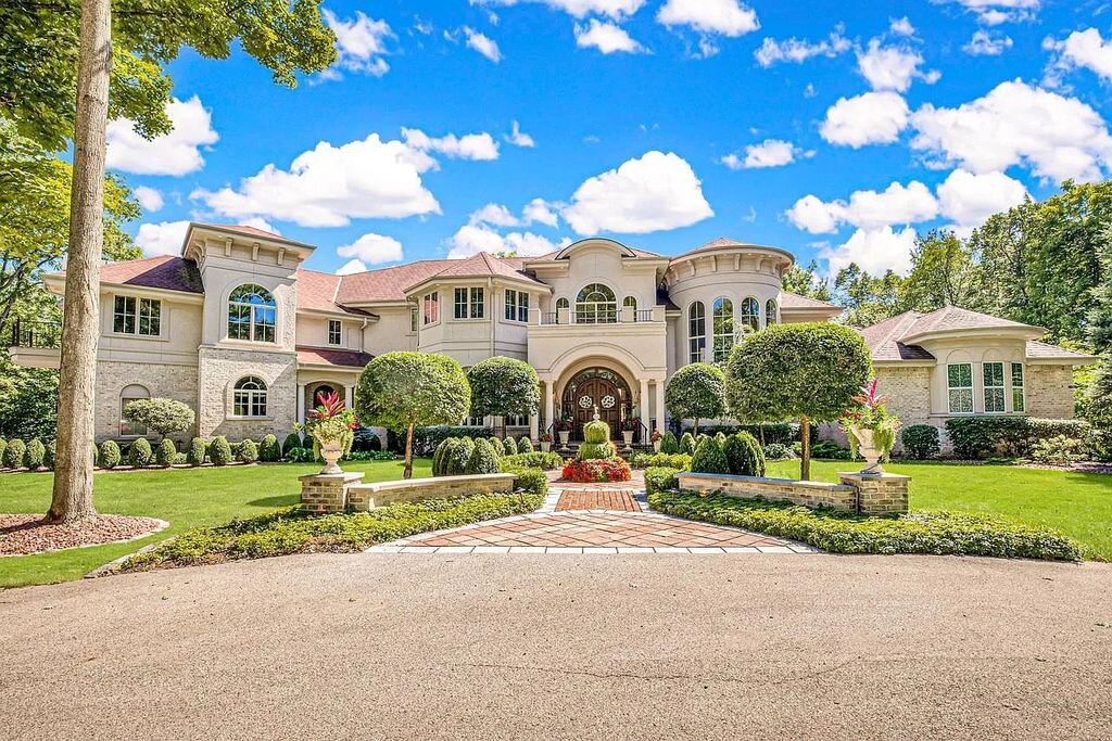 Luxurious estate home in Brookfield, WI featuring elegant architecture, manicured landscaping, and a grand arched entryway under a bright blue sky.