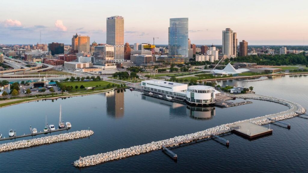 Aerial view of downtown Milwaukee skyline at sunrise, featuring Discovery World, the harbor, and modern high-rise buildings along Lake Michigan.