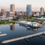 Aerial view of downtown Milwaukee skyline at sunrise, featuring Discovery World, the harbor, and modern high-rise buildings along Lake Michigan.