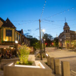 Charming evening street view in downtown Wauwatosa, featuring string lights, historic buildings, and the Village Beer Garden filled with people dining outdoors.