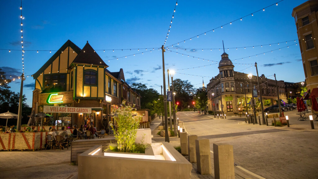 Charming evening street view in downtown Wauwatosa with string lights, historic buildings, and people dining at the Village Beer Garden.