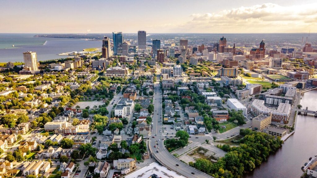 Aerial view of downtown Milwaukee, Wisconsin, showcasing the city skyline, residential neighborhoods, and Lake Michigan in the background.