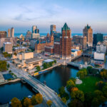 Aerial view of downtown Milwaukee with skyscrapers, the Milwaukee River, and surrounding bridges during early morning light.