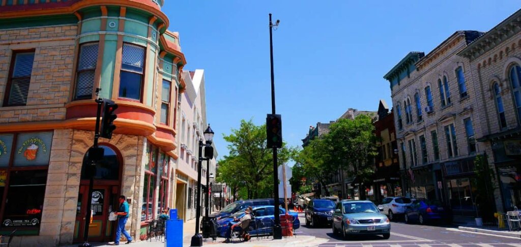 Colorful historic buildings and small businesses line a lively street in downtown Waukesha, Wisconsin, under a bright blue sky.