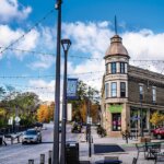 Historic building with turret in Wauwatosa Village, lined with shops, string lights, and autumn trees under a bright blue sky.