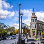 Charming street view of downtown Wauwatosa, featuring historic architecture, string lights, colorful trees, and local shops under a bright blue sky.