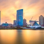 Sunset view of downtown Milwaukee skyline with the Milwaukee Art Museum in the foreground reflecting over calm lake waters.