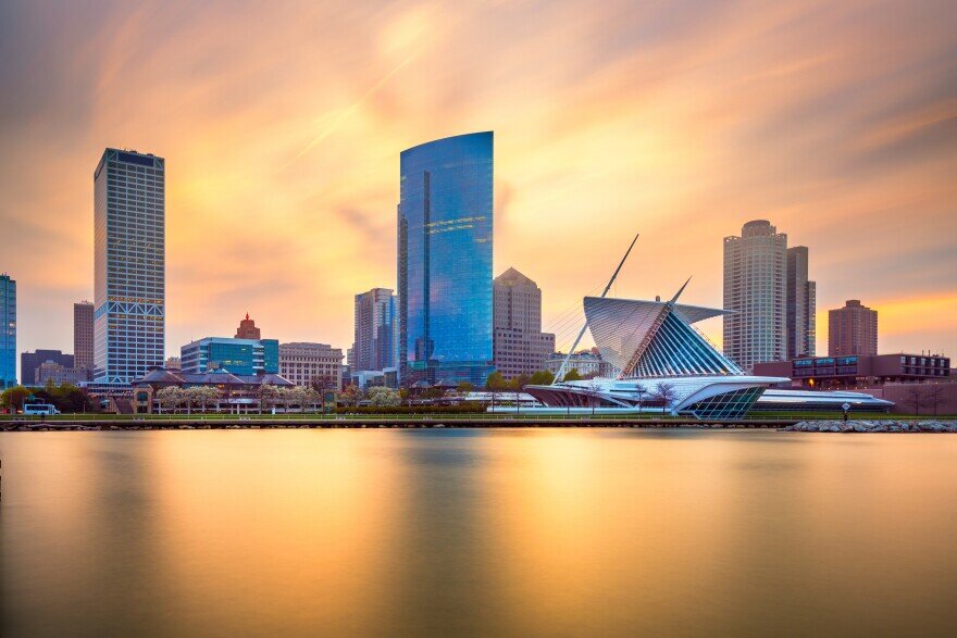 Sunset view of downtown Milwaukee skyline with the Milwaukee Art Museum in the foreground reflecting over calm lake waters.