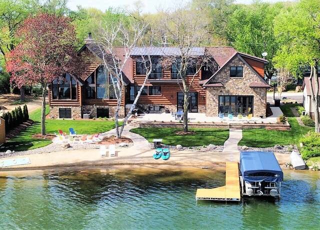 Luxury lakefront home with private dock, outdoor seating, and panoramic windows.