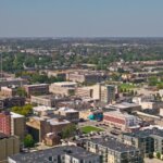 Aerial view of downtown Kenosha, Wisconsin, showcasing mid-rise buildings, residential areas, and green spaces under a clear blue sky.