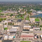 Aerial view of downtown Kenosha, Wisconsin, showing streets, buildings, green spaces, and Lake Michigan shoreline in the background.