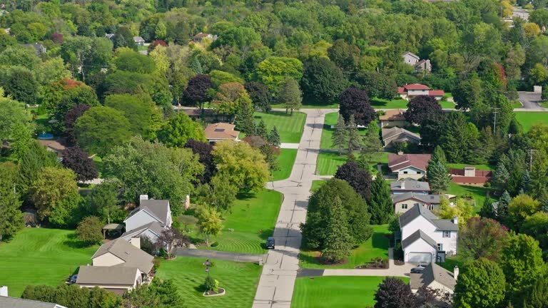 Aerial view of a quiet suburban neighborhood in Brookfield, Wisconsin, featuring tree-lined streets, neatly manicured lawns, and a mix of single-family homes surrounded by dense green foliage during late summer.